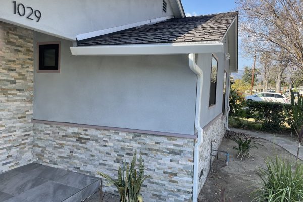 A closeup of the side of a white, two-story house. The focal point of the image is the white rain gutters running along the side of the house.