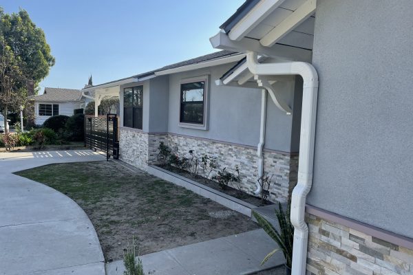 A side angle of a one story white home with a set of bright white rain gutters running along the corner.