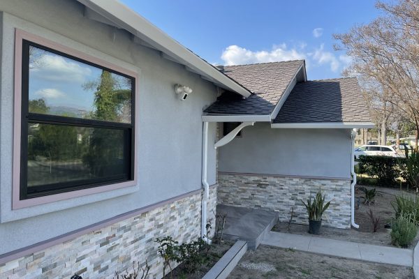 A side view of a one story home with a single window and white rain gutters running along the roof.